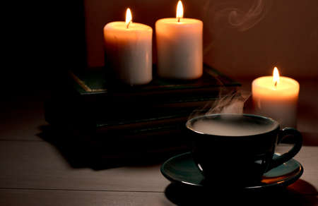 Cup of hot coffee with green smoke, books and burning candles. Desk table in power supply cutの写真素材