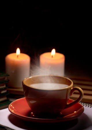 Hot yellow mug with drink, steam and two burning candles together on the table, black background space for text.の写真素材