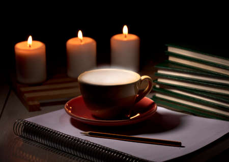 table with burning candles notebook pencil books, yellow mug with steam smokeの写真素材