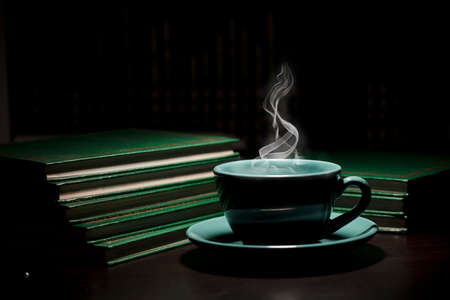 table with green cup of hot coffee, with books, black background, space for text.の写真素材