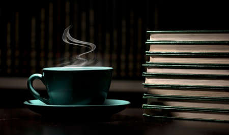 table with green cup of hot coffee, with books, black background, space for text.の写真素材
