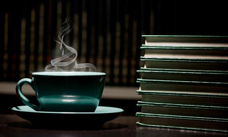 table with green cup of hot coffee, with books, black background, space for text.の写真素材