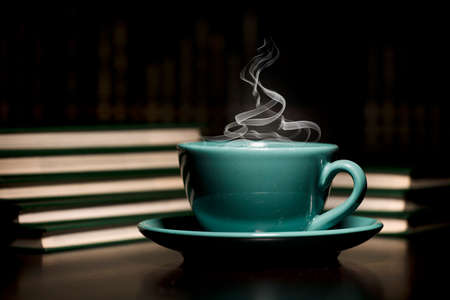 table with green cup of hot coffee, with books, black background, space for text.の写真素材