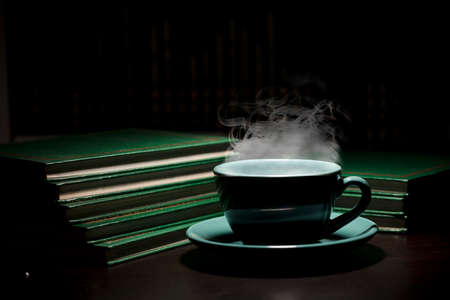 table with green cup of hot coffee, with books, black background, space for text.の写真素材