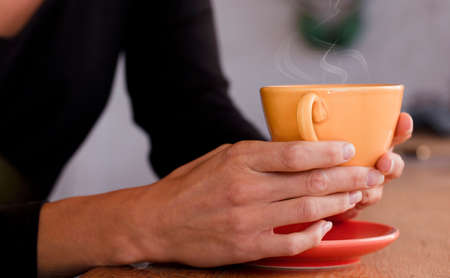 Female hands hold a yellow cup with coffee. Focus on the cupの写真素材