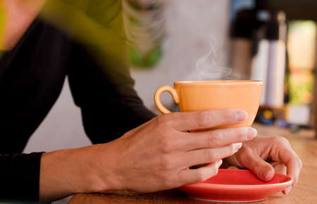 Female hands hold a yellow cup with coffee. Focus on the cupの写真素材