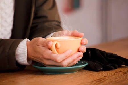She warms her hands with a cup of hot coffee.の写真素材