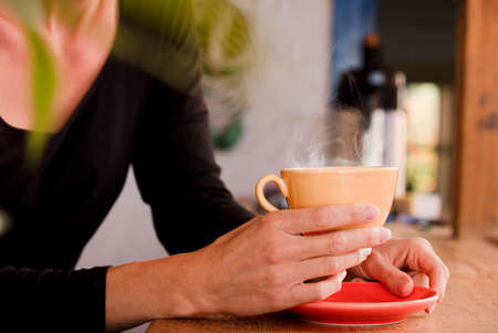 Female hands hold a yellow cup with coffee. Focus on the cupの写真素材