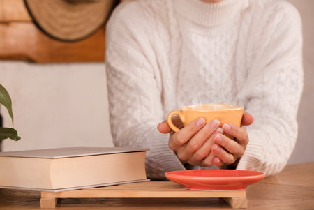 Close up of female hands with a cup of drinks. Beautiful girl in white sweater holding a yellow cup of tea or coffee in the Focus on the cup.の写真素材
