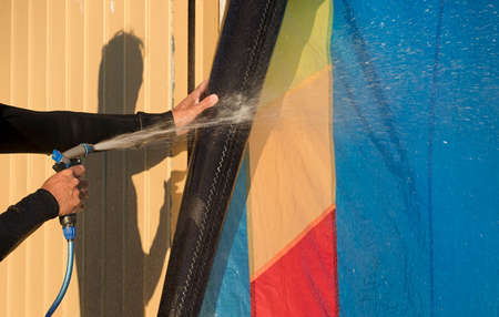 man cleans wingfoil sports equipment, with pressurized water hoseの写真素材