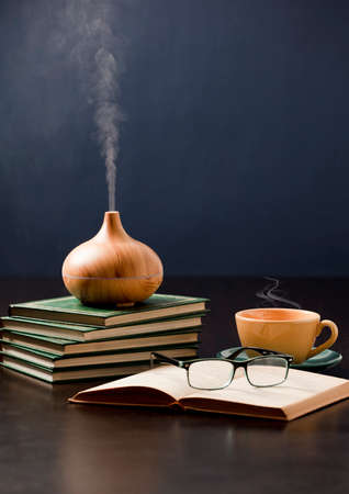 Relaxation at home with aromatherapy oil diffuser, yellow tea cup, book, reading glasses. Aroma essence of health, wellness aromatherapy home aromatic tranquil therapyの写真素材