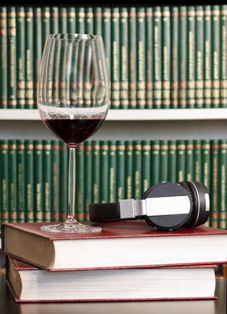 Glass of red wine with headphones on leather surface with library in the background.の写真素材
