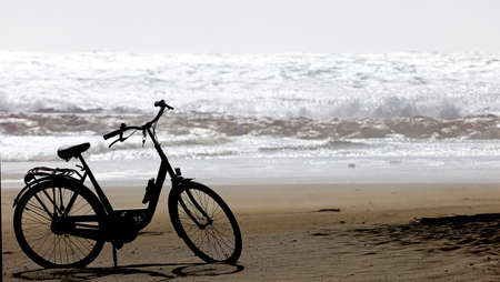 Abandoned bicycle on the sand, strong sea bottom and big waves.の写真素材
