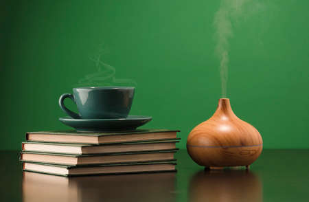 electric ultrasonic humidifier emitting atomized water droplets on a green background, with pile of books. The device is round in shape with a wooden body.の写真素材
