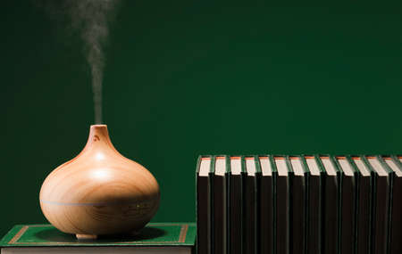electric ultrasonic humidifier emitting atomized water droplets on a green background, with pile of books. The device is round in shape with a wooden body. Greenの写真素材