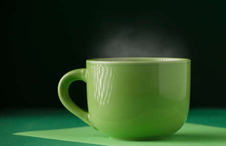 Cup of green tea or coffee, hot with steam, dark green background.の写真素材