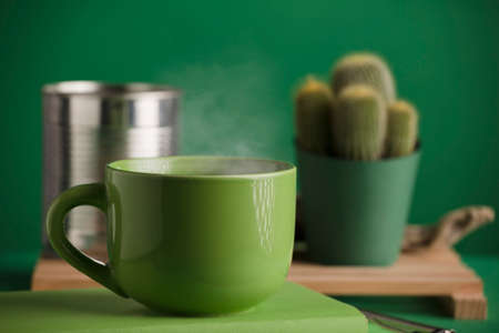 cup of green tea or coffee, hot with steam, cactus and recycled metal can, green background.の写真素材
