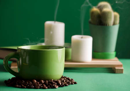 cup of hot green coffee with steam and beans, cactus, extinguished candles with smoke, dark green background.の写真素材