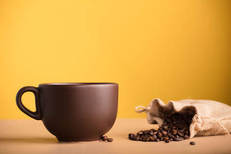 brown cup with coffee and raffia sack with roasted coffee beans, with yellow backgroundの写真素材