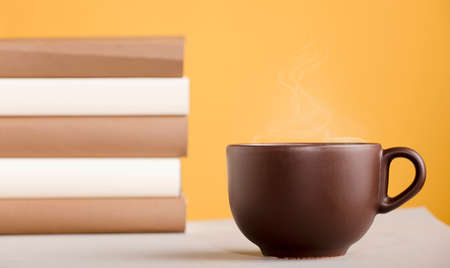 Brown cup of coffee or tea with hot steam, on the table, with booksの写真素材