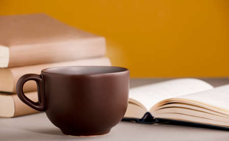 desk with cup of coffee or tea with hot steam, open books, orange yellow backgroundの写真素材