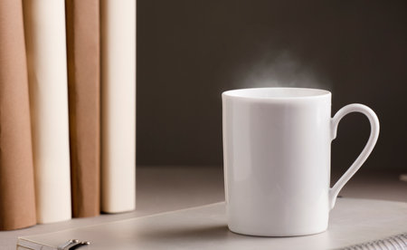 white cup of coffee with hot steam, on the desk with books, gray backgroundの写真素材