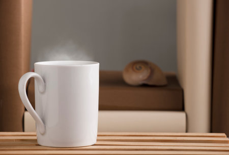 white cup of coffee with hot steam, on the desk with nautilus shell and books, gray backgroundの写真素材