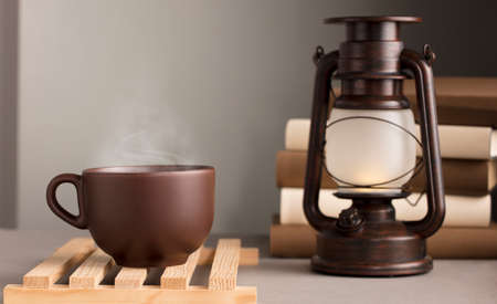 brown cup of coffee with hot steam, on desk with sunlight lamp, gray backgroundの写真素材