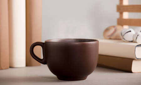 brown cup of coffee with hot steam, on the desk with shells and books, gray backgroundの写真素材