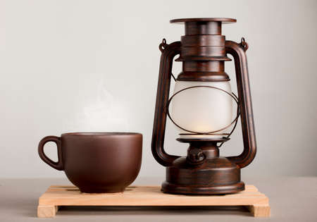 brown cup of coffee with hot steam, on desk with sunlight lamp, yellowish orange backgroundの写真素材
