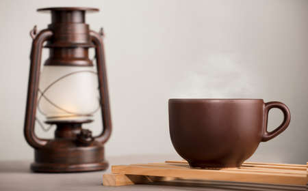 brown cup of coffee with hot steam, on desk with sunlight lamp, white gray backgroundの写真素材