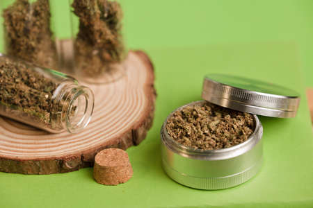 marijuana on grinder, glass jars on table, with dark green background.