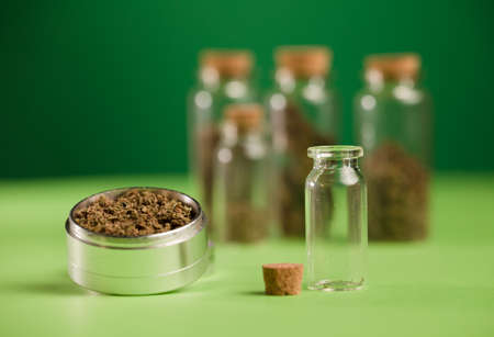 chopped marijuana in a grinder, and airtight glass jars with different types of cannabis and green books, a process for the production of pure marijuana. green backgroundの写真素材
