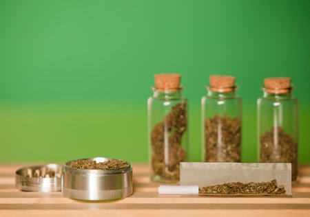 chopped marijuana, on cigarette paper with a filter and airtight glass jars with different types of cannabis on wood, with grinder process for the production of marijuana cigars. green background.の写真素材