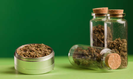 marijuana on grinder, glass jars on table, with dark green background.の写真素材