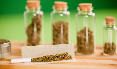 chopped marijuana, on cigarette paper with a filter and airtight glass jars with different types of cannabis on wood, with grinder process for the production of marijuana cigars. green background.の写真素材