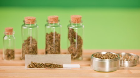 chopped marijuana, on cigarette paper with a filter and airtight glass jars with different types of cannabis on wood, with grinder process for the production of marijuana cigars. green background.の写真素材