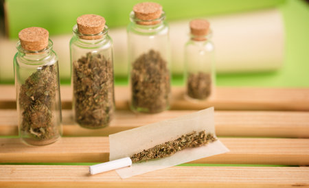 chopped marijuana, on cigarette paper with a filter and airtight glass jars with different types of cannabis on wood, process for the production of marijuana cigars. green background.の写真素材