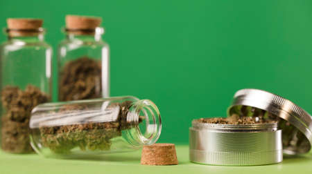grinder with marijuana and glass jars with cork stopper marijuana stored indoors, green background.の写真素材