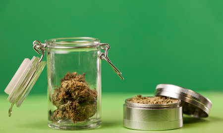 grinder with marijuana and glass jars with cork stopper marijuana stored indoors, green background.の写真素材
