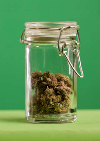 glass jar with airtight seal and marijuana stored inside, green background.の写真素材