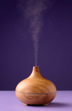Essential oil air freshener in wood with steam, with a violet background (very peri).の写真素材