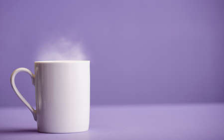 White ceramic cup of coffee or tea with hot steam, with a purple background (very peri).の写真素材