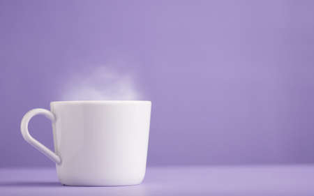 White ceramic cup of coffee or tea with hot steam, with a purple background (very peri).の写真素材