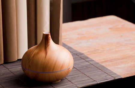 Essential oil air freshener on wood, with books on table, brown background.の写真素材