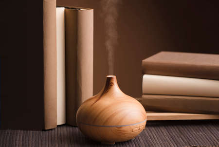 Essential oil air freshener on wood, with books on table, brown background.の写真素材