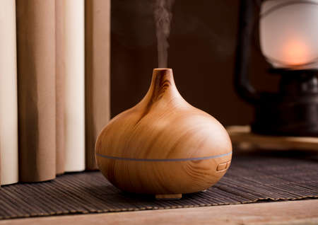 Essential oil freshener on wood, with books and lamp, on table, brown background.の写真素材