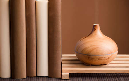Essential oil air freshener on wood, with books on table, brown background.の写真素材