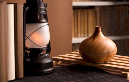 Essential oil freshener on wood, with books and lamp, on table, brown background.の写真素材
