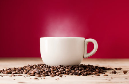 broken white coffee cup with hot steam smoke and beans on wooden table, red backgroundの写真素材